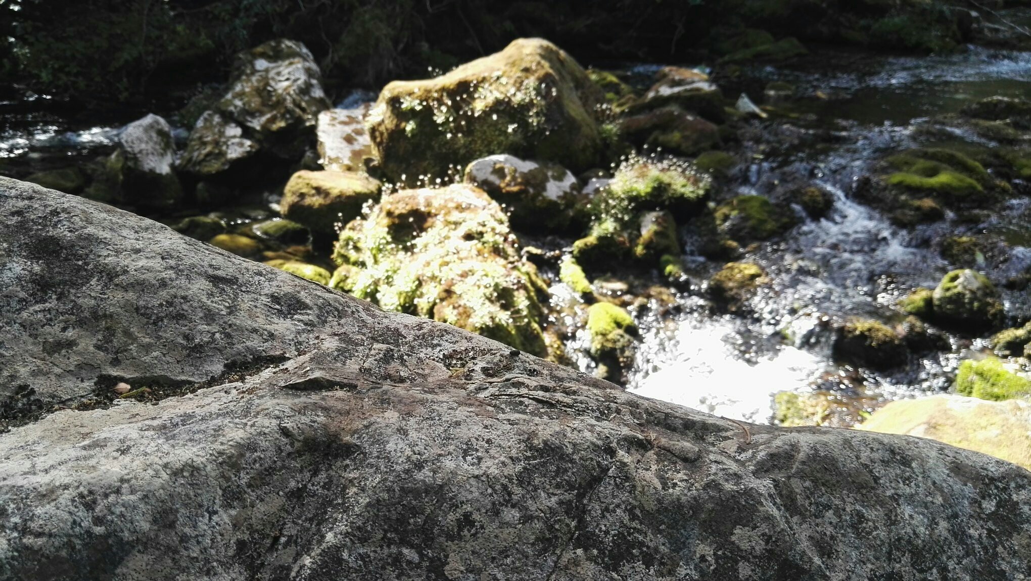 A picture of a rock with a small river behind.